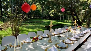 A long dining table set outdoors with white chairs, gold-rimmed plates, and candles. - Brookside Lodge B&B (Matsapha)