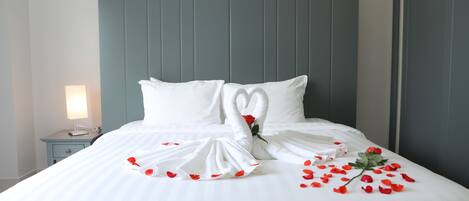 A neatly made bed with a heart-shaped towel arrangement and scattered rose petals.