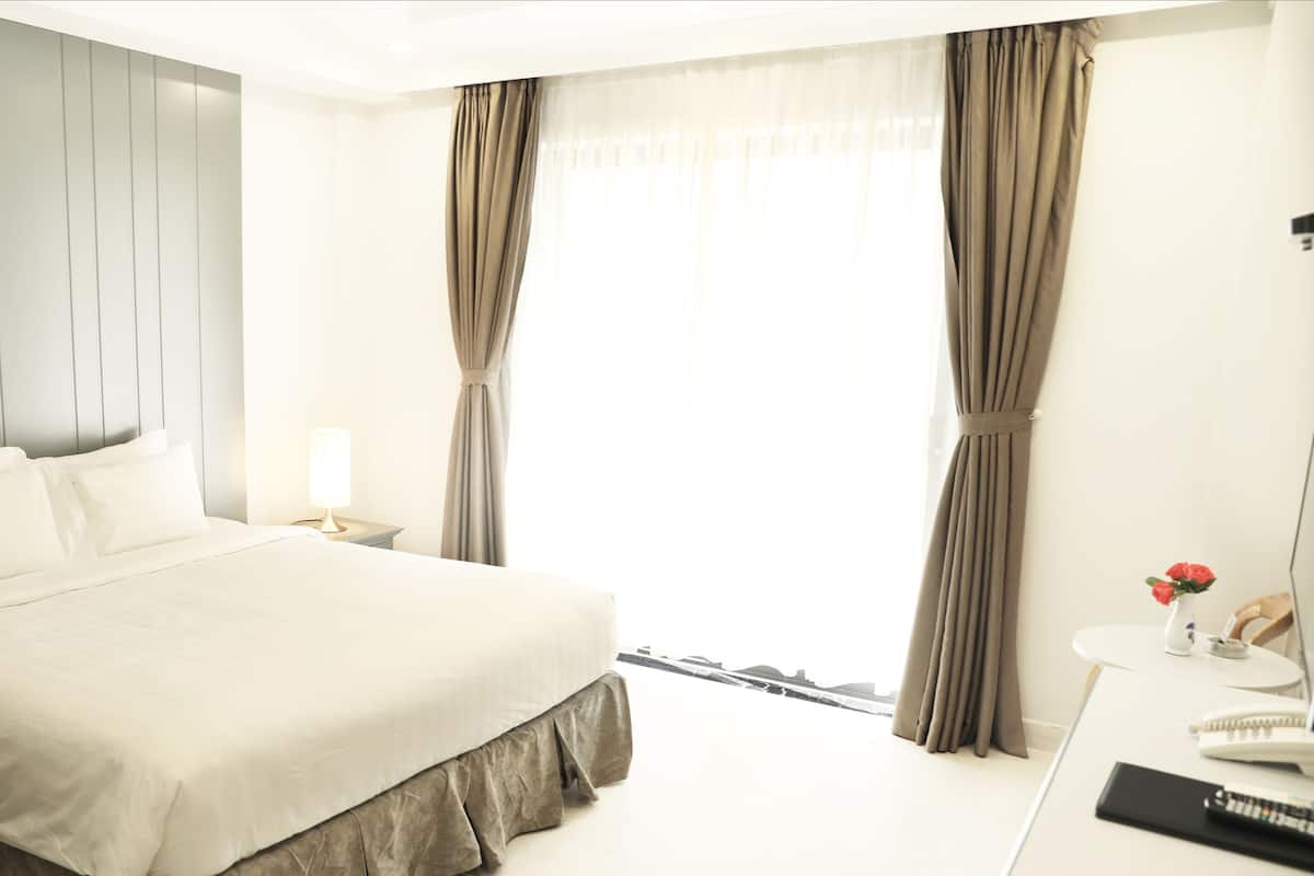 Quarto de hotel com cama, mesa de cabeceira, luminária e escrivaninha com cadeira.