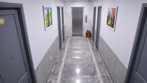 A hallway with marble flooring, grey doors, and framed artwork on the walls. - Fide Hotel (Ho Chi Minh City)