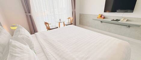 A hotel room with a large bed, a desk, a chair, a TV, and a window with curtains.