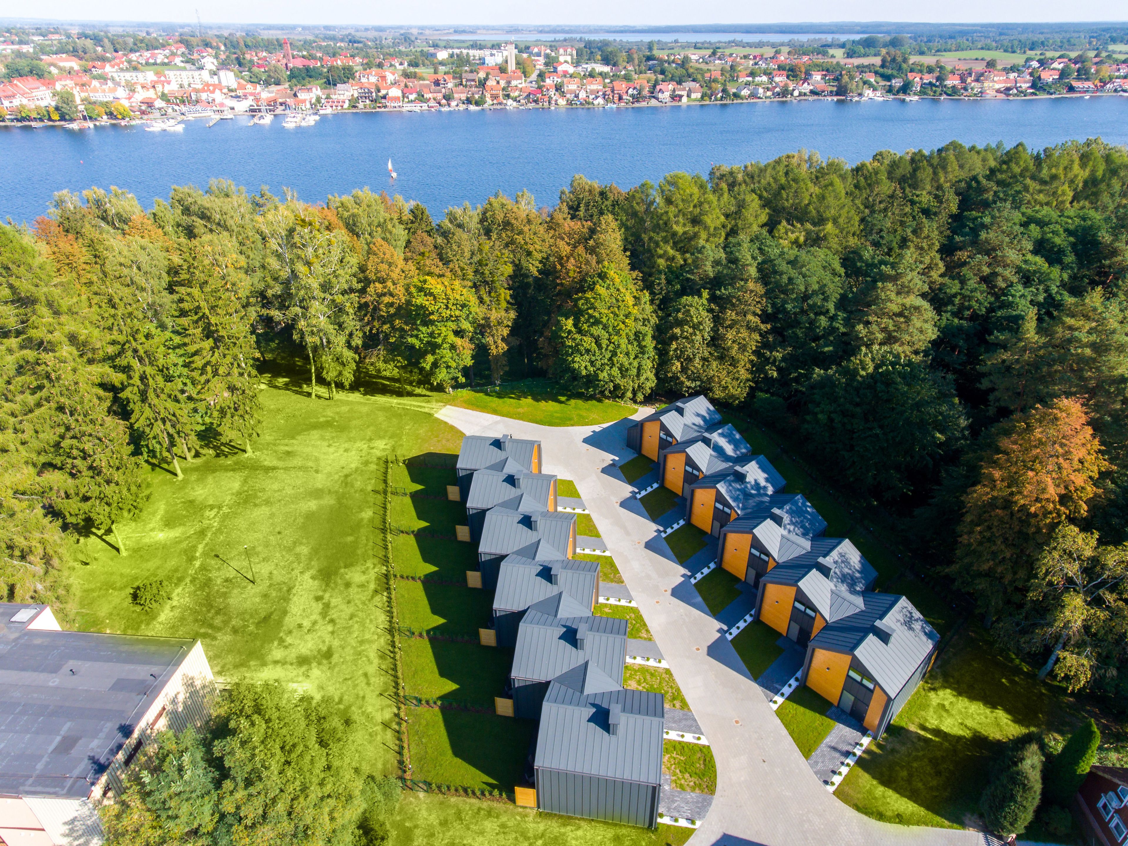 A residential area with modern houses arranged in a row, a clear road, and a lake in the background.