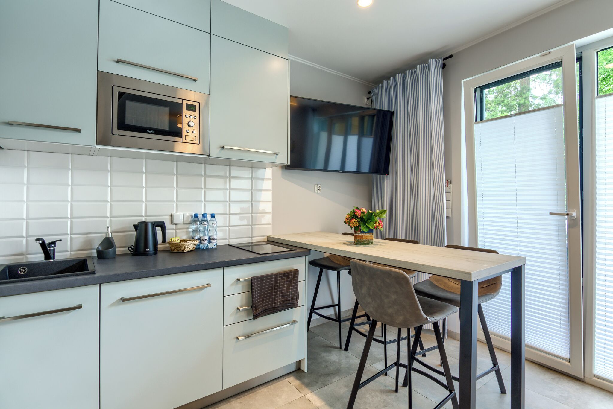 A modern kitchen with a microwave, sink, and bar stools.