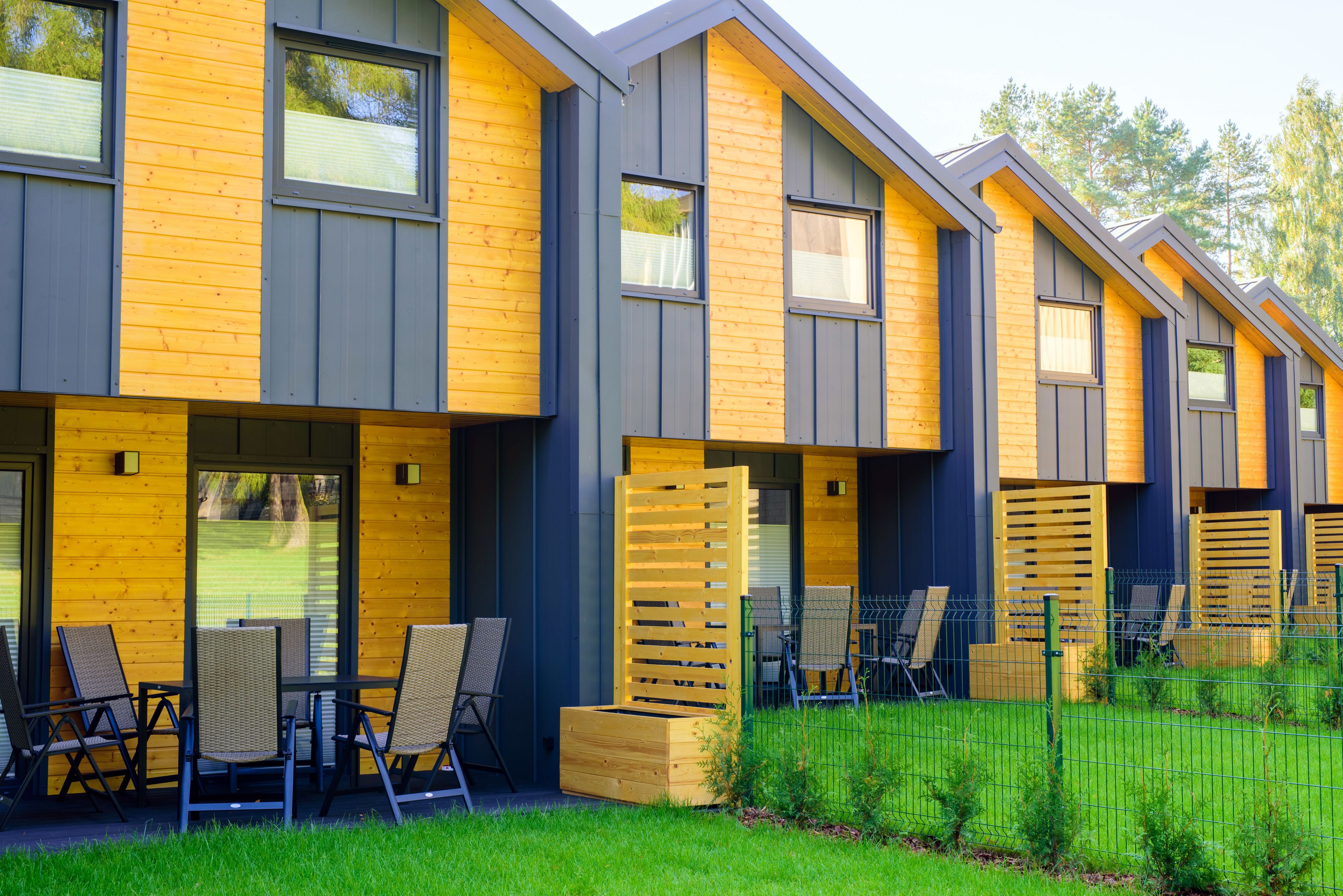 Une rangée de chalets modernes aux façades en bois et aux grandes fenêtres, dotés d’un espace salon extérieur et bordés d’une pelouse verdoyante.
