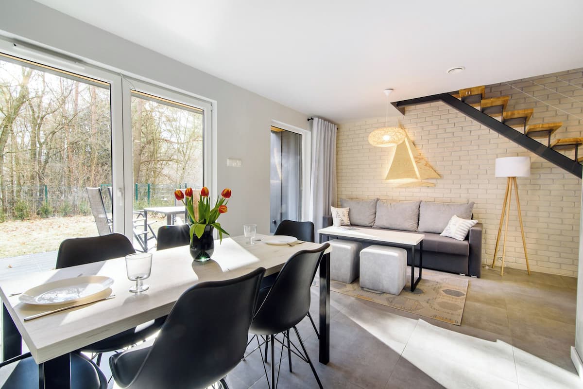 Ein modernes Wohnzimmer mit Sofa, Esstisch und Stühlen. Eine Treppe mit Holzvertäfelung und einer Wandleuchte.