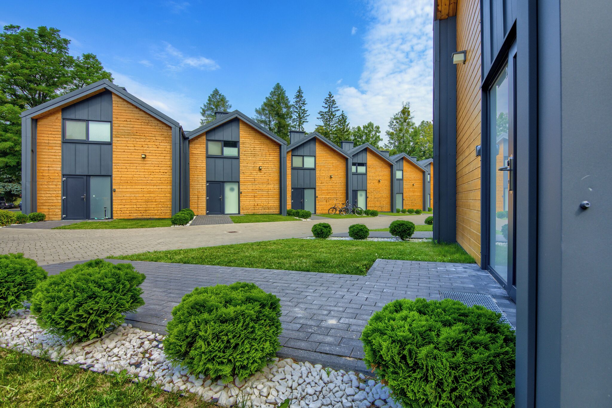A row of modern wooden cabins with grey roofs, arranged in a straight line along a paved pathway.