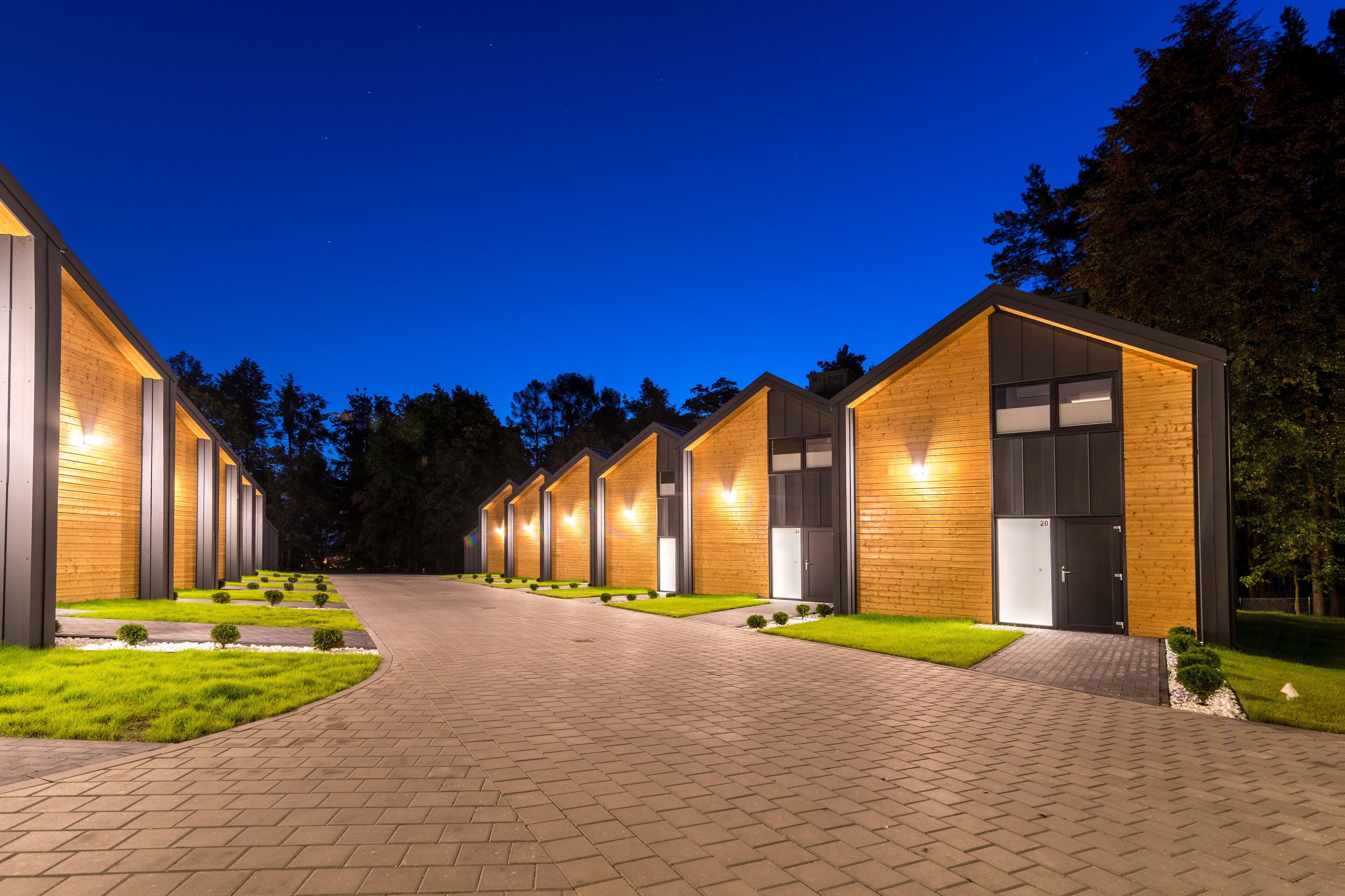 A row of modern, well-lit cabins with a paved walkway and manicured lawns.