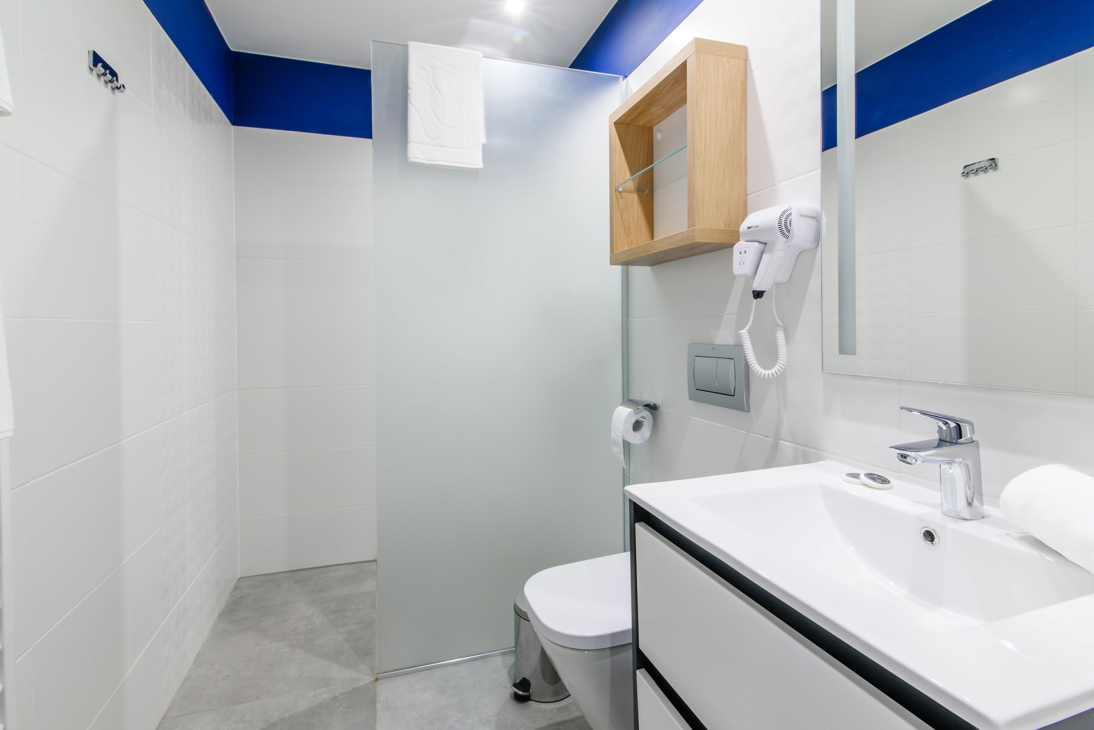 A modern bathroom with a white sink, a mirror, a towel hanging on the wall, and a shower area.