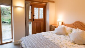 Una camera da letto con una porta in legno, un letto con biancheria da fiori, un comodino con una lampada e vista su un giardino tramite una porta vetrata.