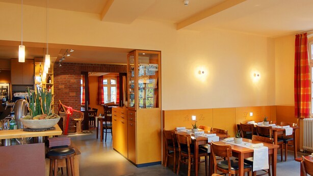 A restaurant with wooden tables and chairs, a brick wall, and a large window with red curtains. - Alte Schule (Reichenwalde)