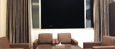 Une pièce dotée d’une grande fenêtre, de deux canapés en cuir marron, d’une table basse en bois et d’une petite lampe de table blanche.