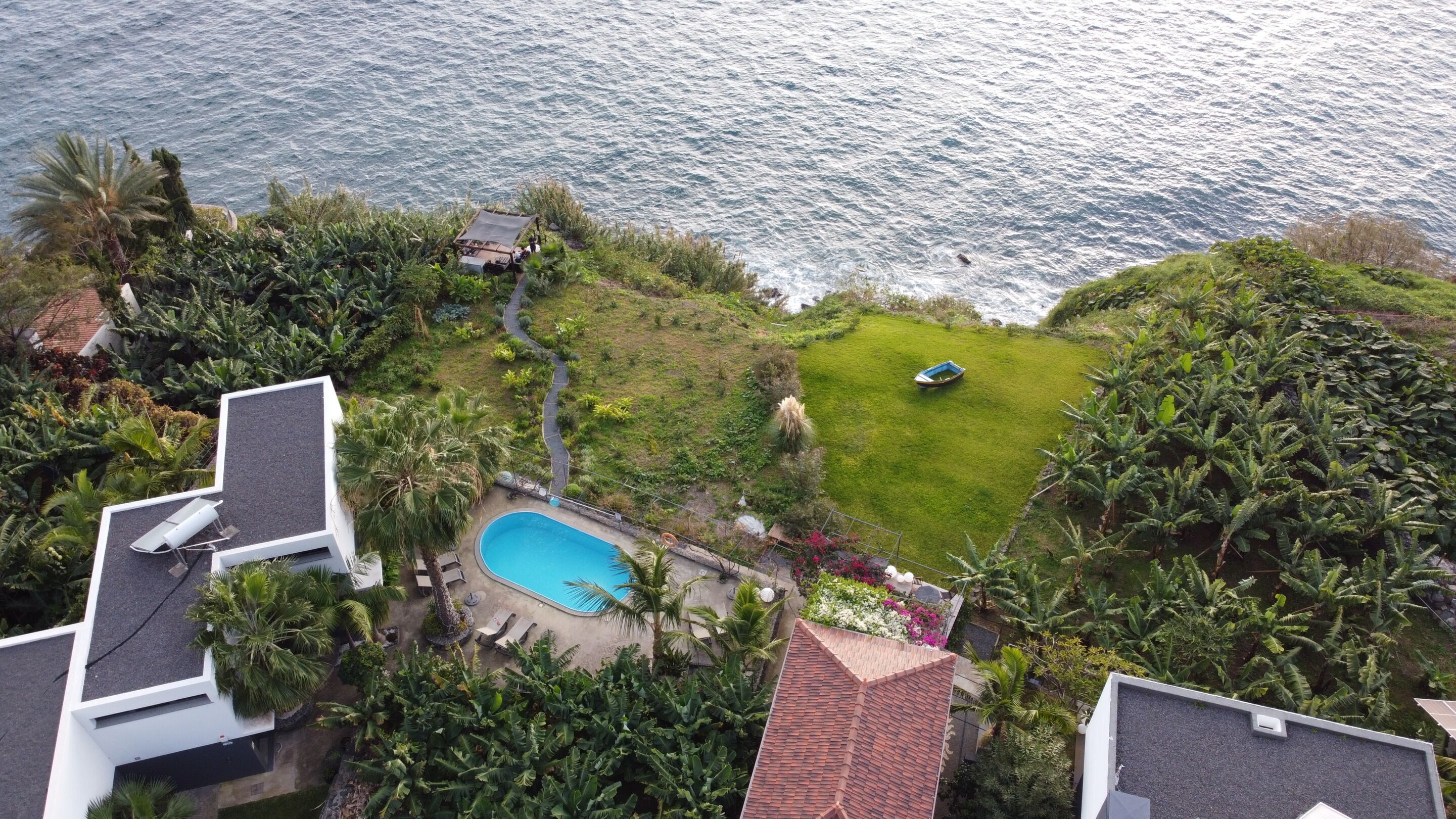 A residential property with a swimming pool, lush greenery, and a view of the sea.