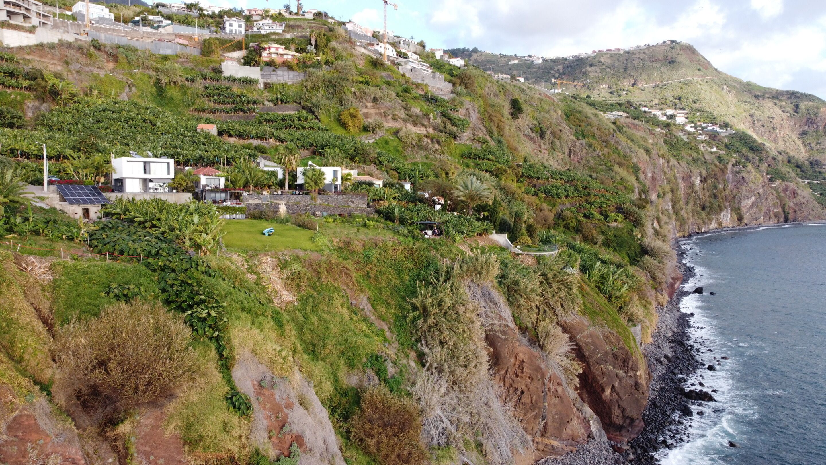 Un turó costaner amb edificis residencials, una zona verda i un litoral rocos.