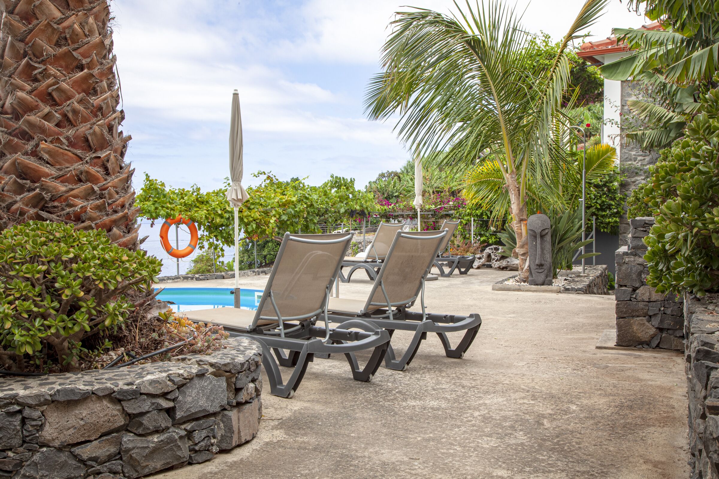 A poolside area with lounge chairs, a lifebuoy, and a stone wall.