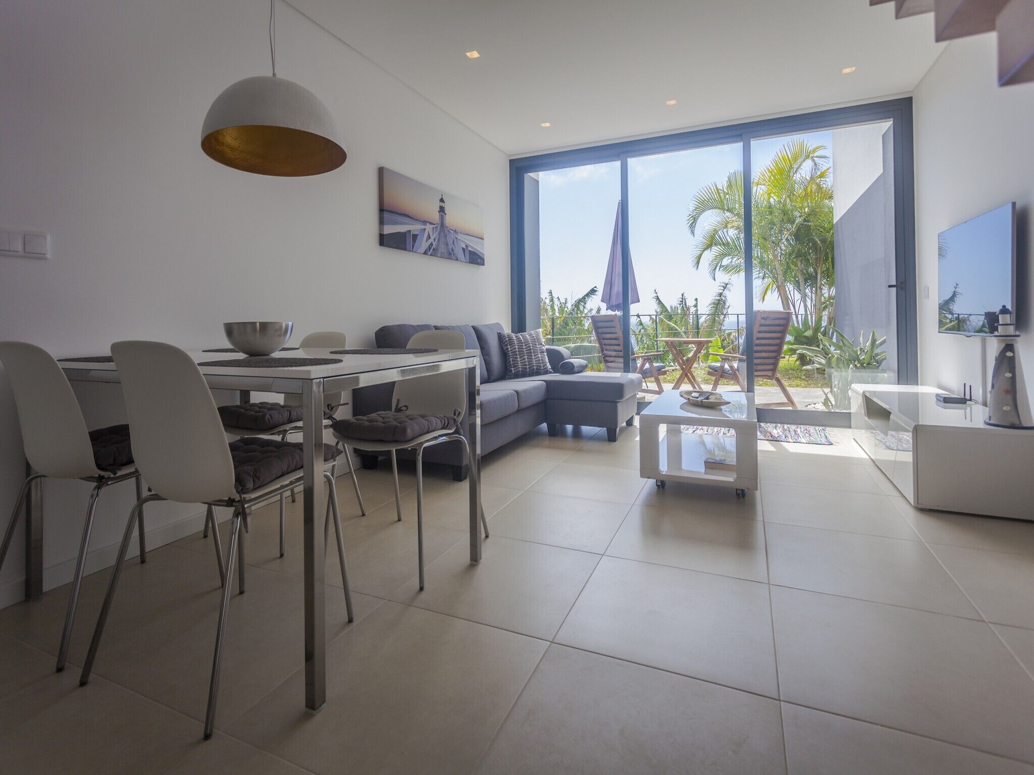 A modern living room with a dining area, large windows, and a view of palm trees.