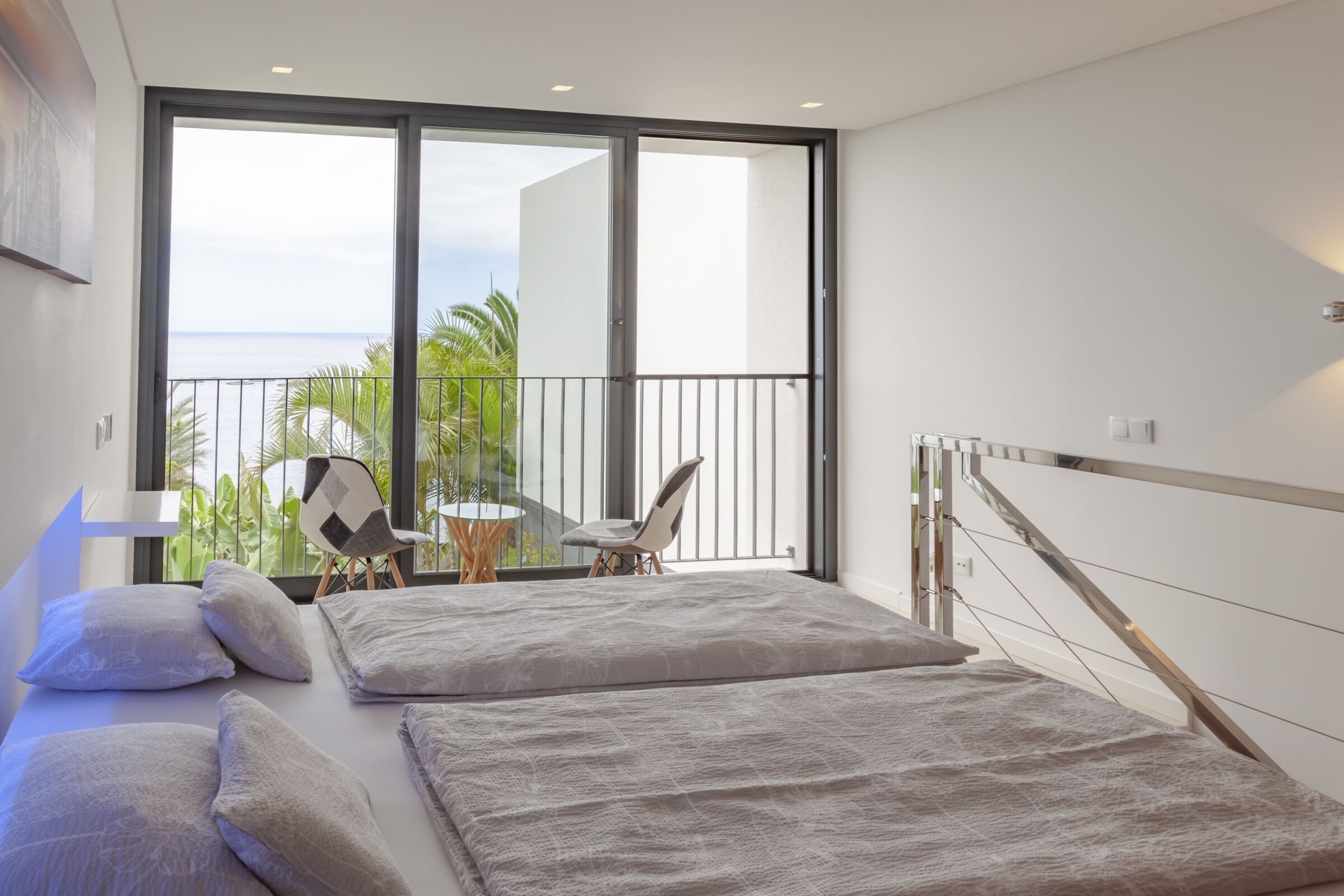 Quarto moderno com uma cama grande, varanda com vista para o mar e uma mesa pequena com cadeiras.