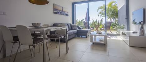 A modern living room with a dining area, large windows, and a view of palm trees.