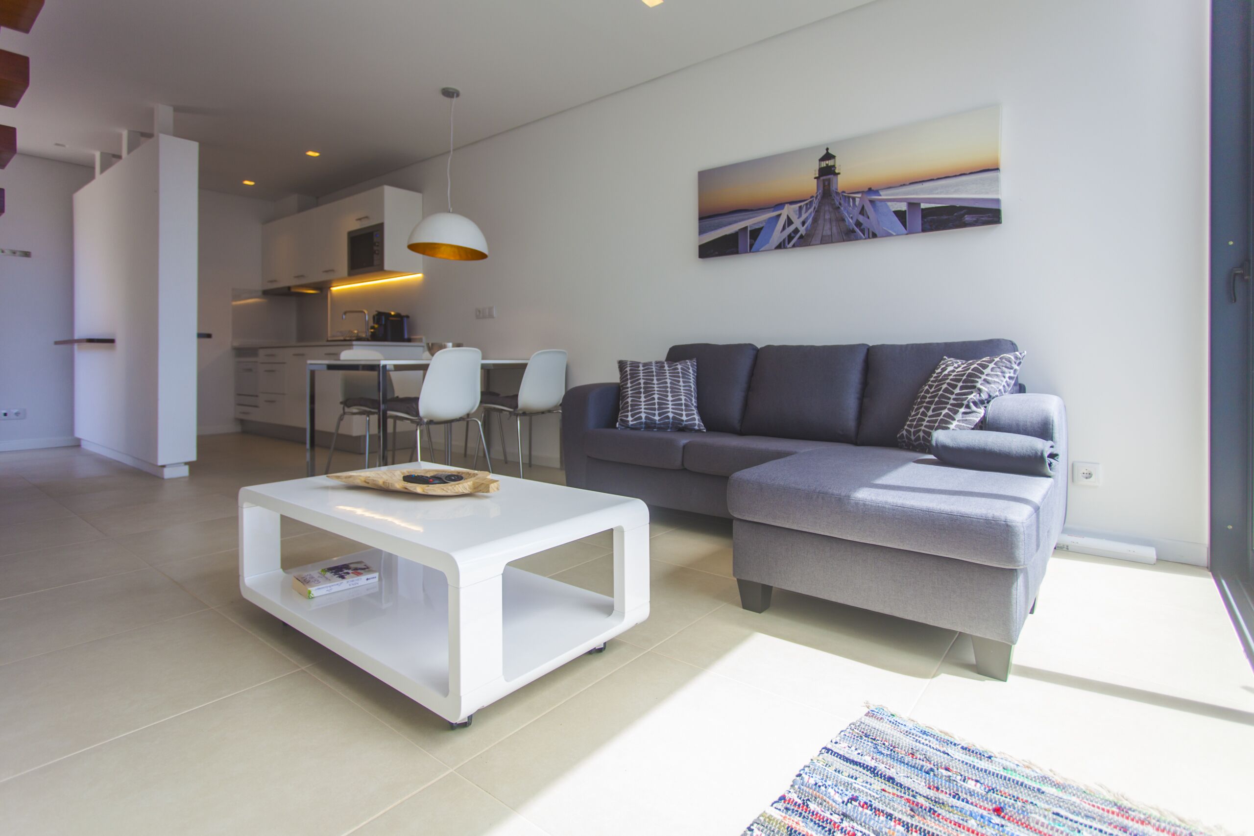A modern living room with a grey sofa, a white coffee table, and a painting of a bridge.