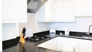 Uma cozinha moderna com armários brancos, bancada preta, fogão a gás e cafeteira.