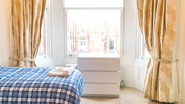 Quarto com cama, penteadeira e janela com cortinas.