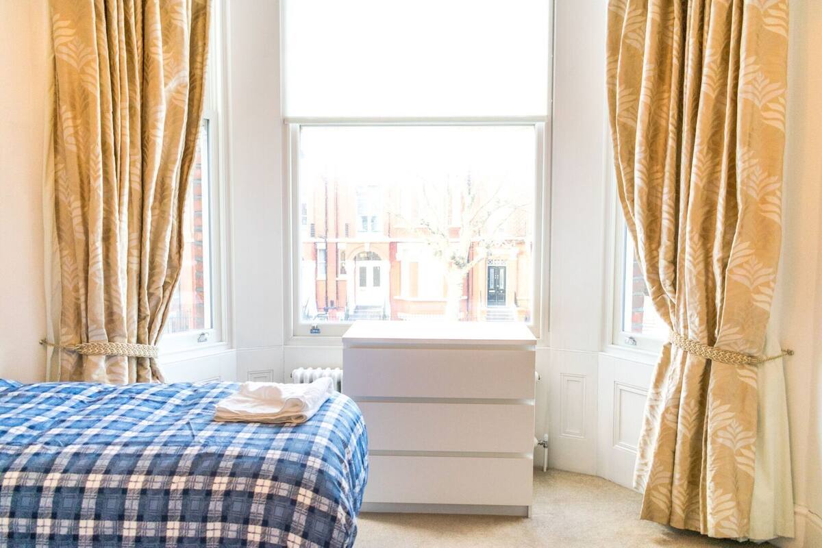 A bedroom with a bed, a dresser, and a window with curtains.