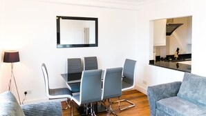 Uma sala de estar moderna com uma mesa de jantar e quatro cadeiras, um sofá, uma luminária e uma área de cozinha com fogão e armários.