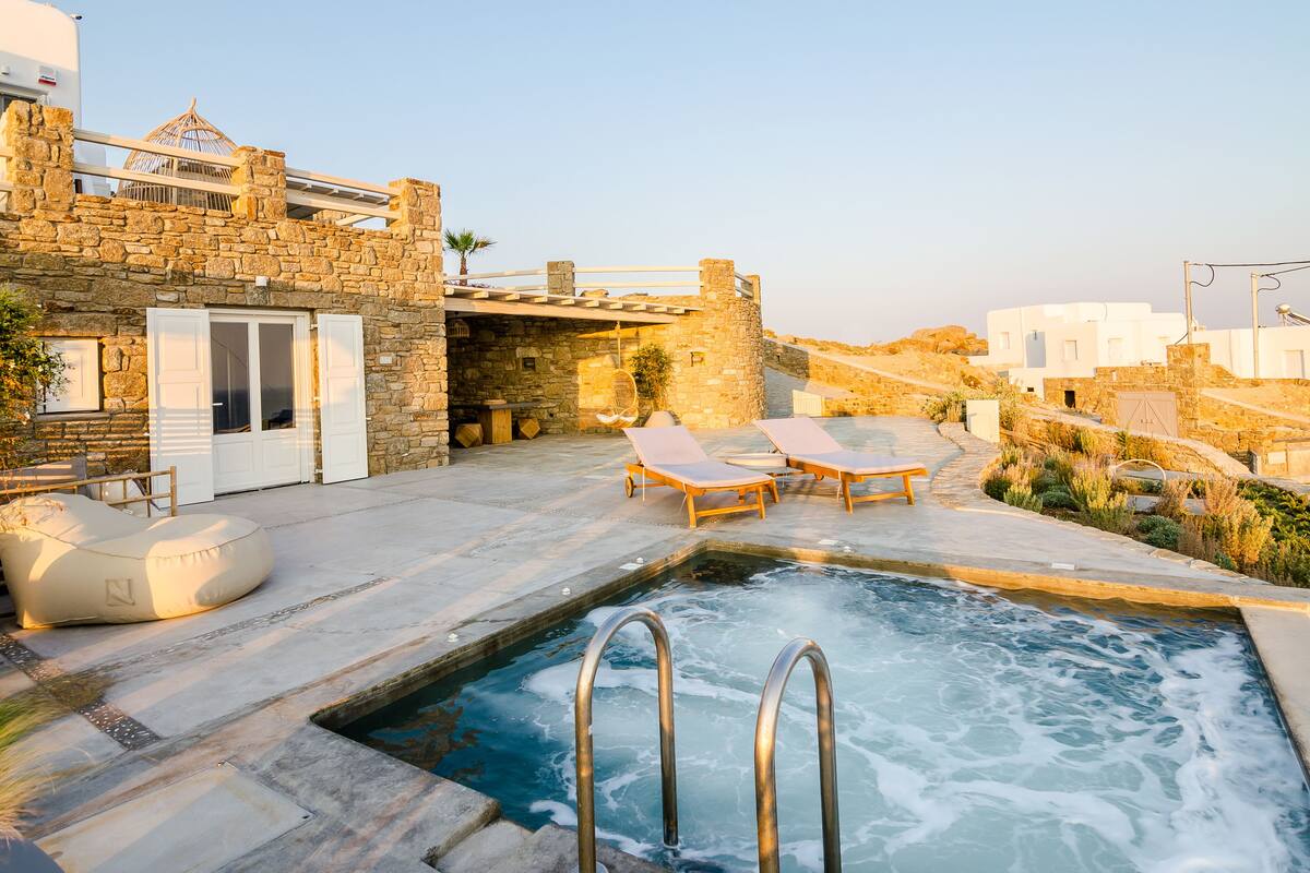 A stone building with a pool, lounge chairs, and a small garden area.