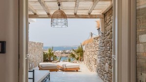 A narrow corridor with a stone wall, a bed, a bench, and a hanging light fixture. - Eden View Suites & Villas (Mykonos)