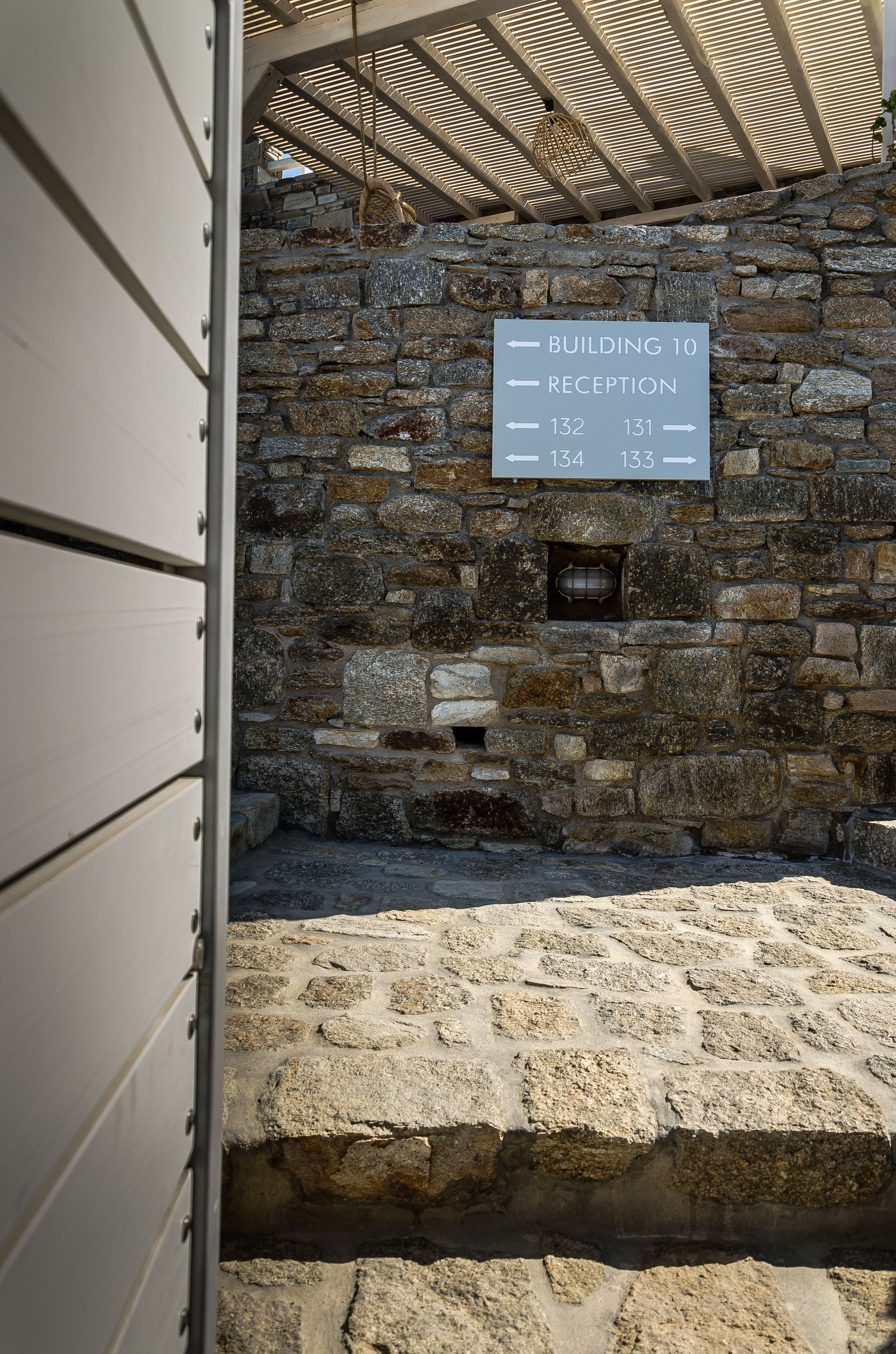 Un mur de pierre sur lequel est apposée une plaque indiquant le bâtiment numéro 10, l’accueil, ainsi que les numéros des salles 132 et 133.
