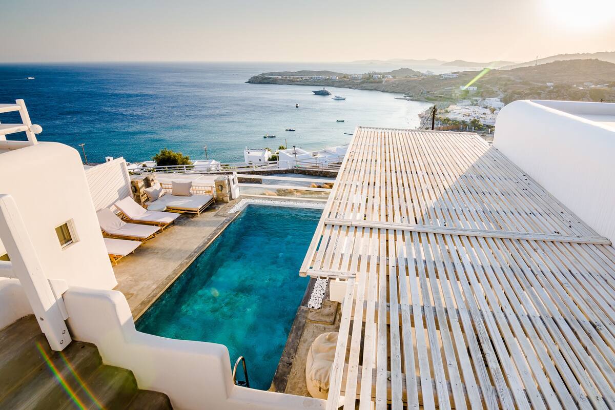 A rooftop pool with white lounge chairs and a view of the sea.