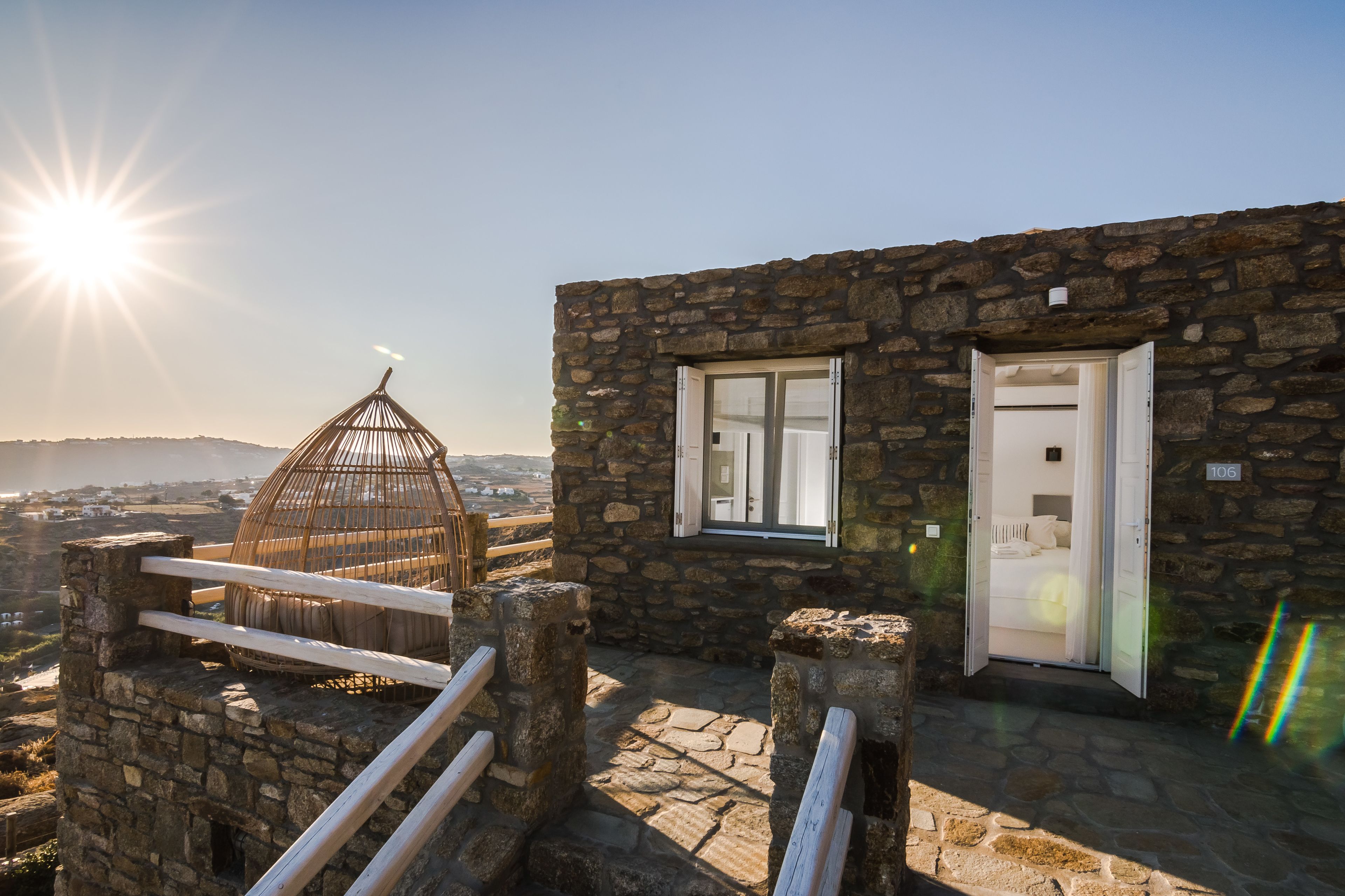 Un edificio de piedra con un gran ventanal y una puerta, baranda de madera y vistas del paisaje.