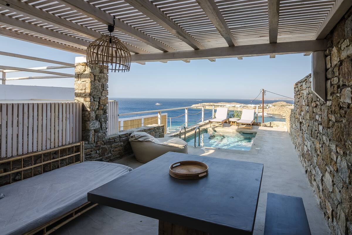 A balcony with a stone wall, a pool, and a view of the sea.