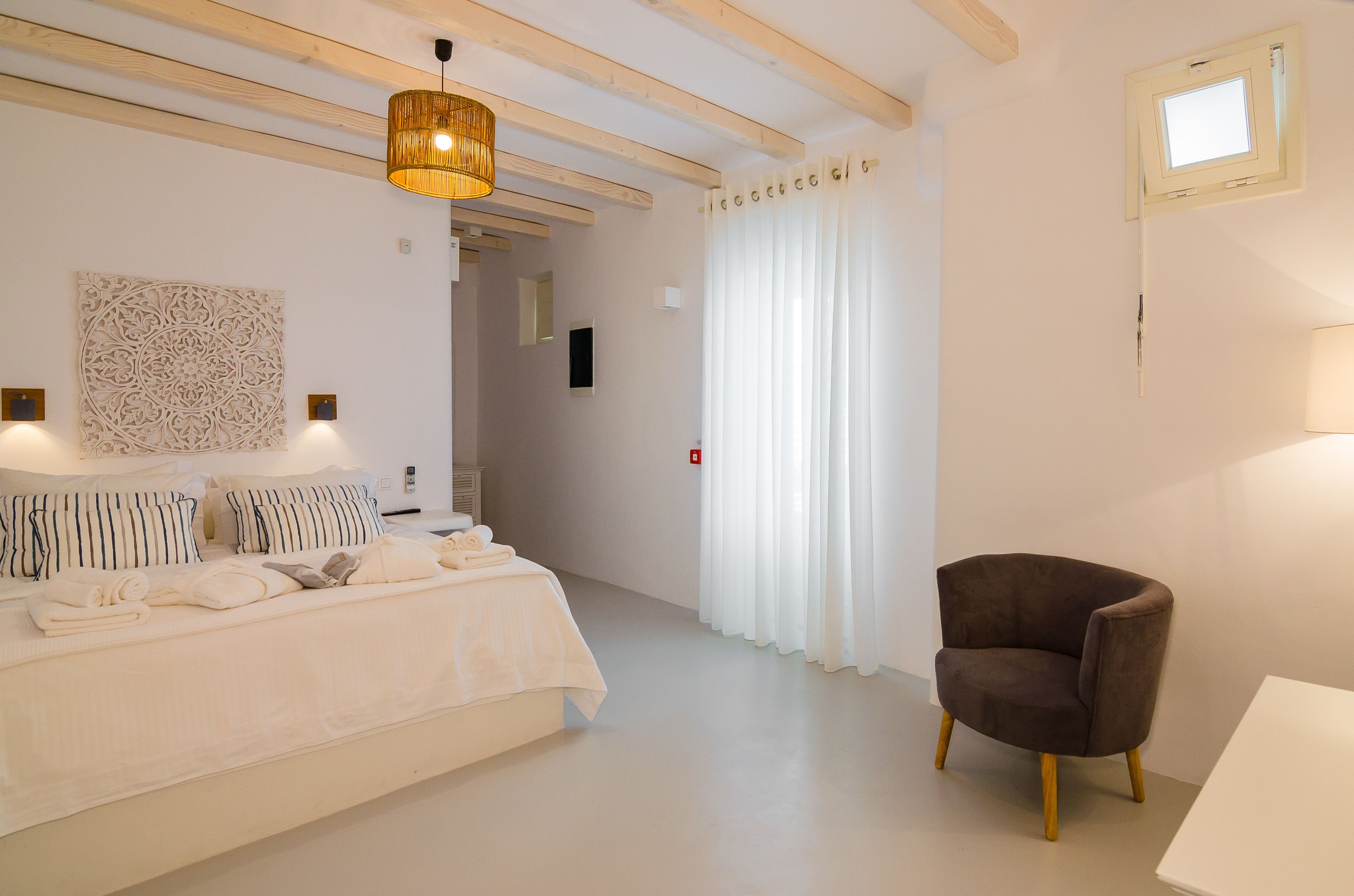 Un dormitorio con una cama, una silla, un candelabro colgante y una ventana con cortinas.