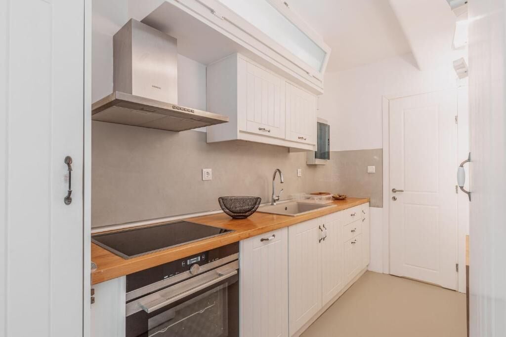 A modern kitchen with white cabinetry, a built-in oven, and a stainless steel range hood.