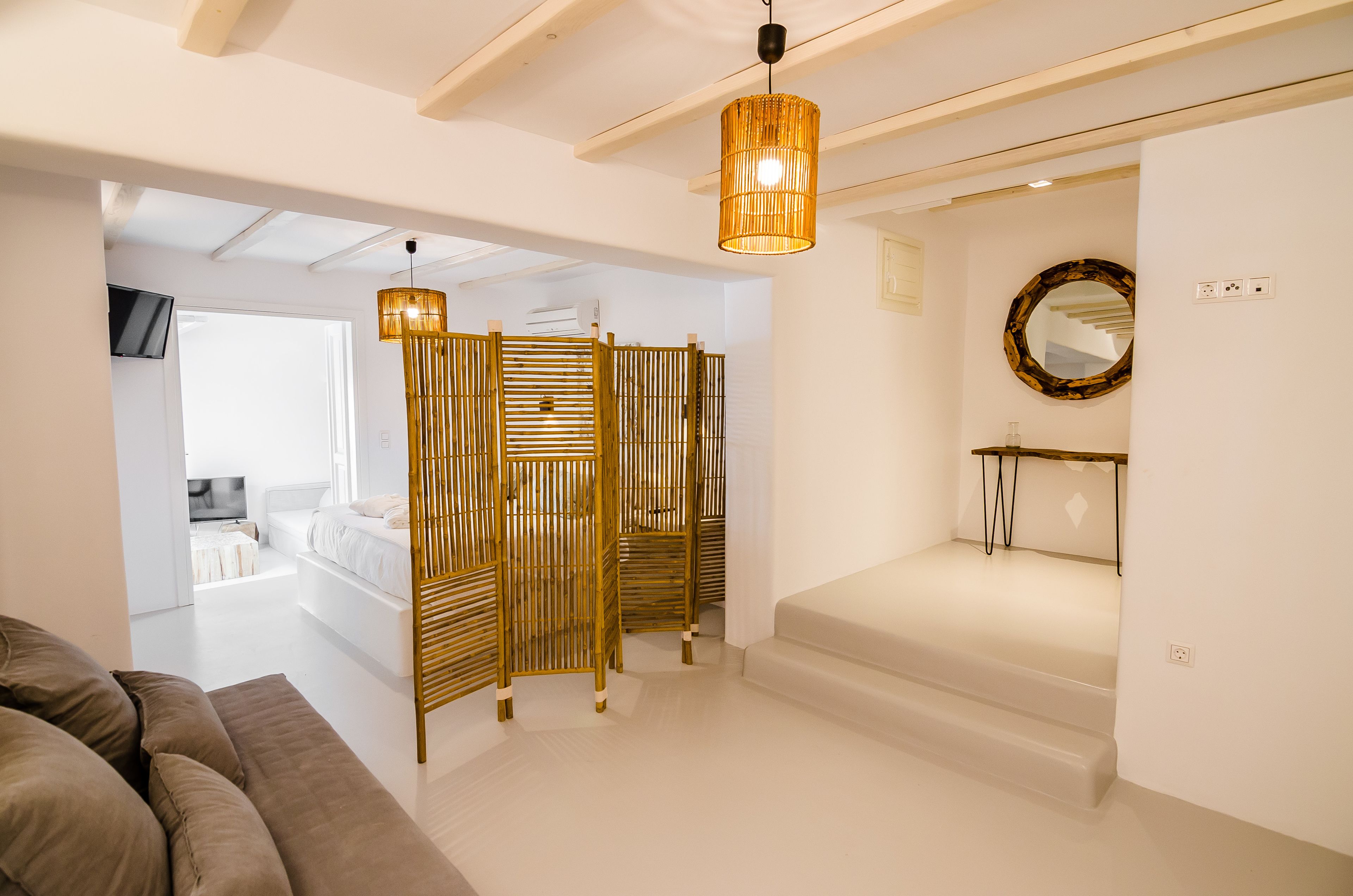 A modern hotel room with a sofa, a bed, a wooden partition, and a hanging light fixture.
