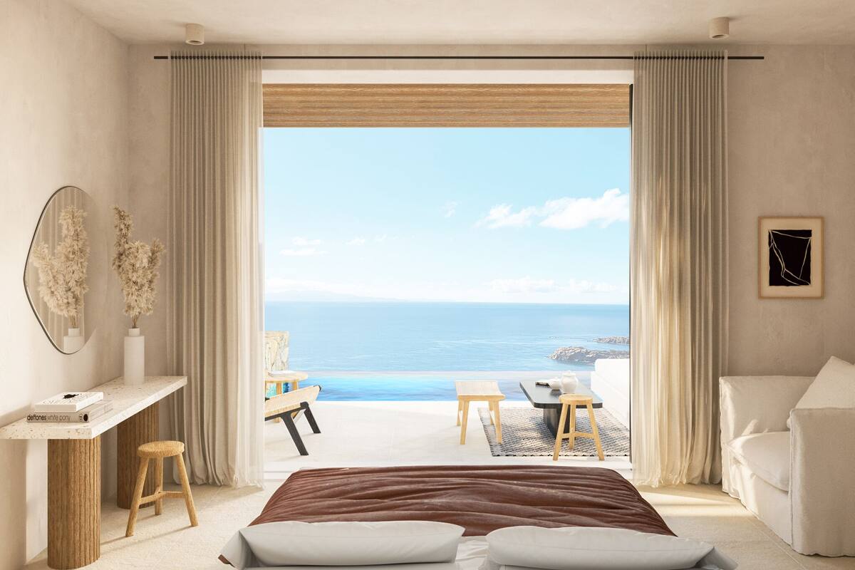 A bedroom with a large bed, a desk, and a chair, with a view of the sea and a balcony.