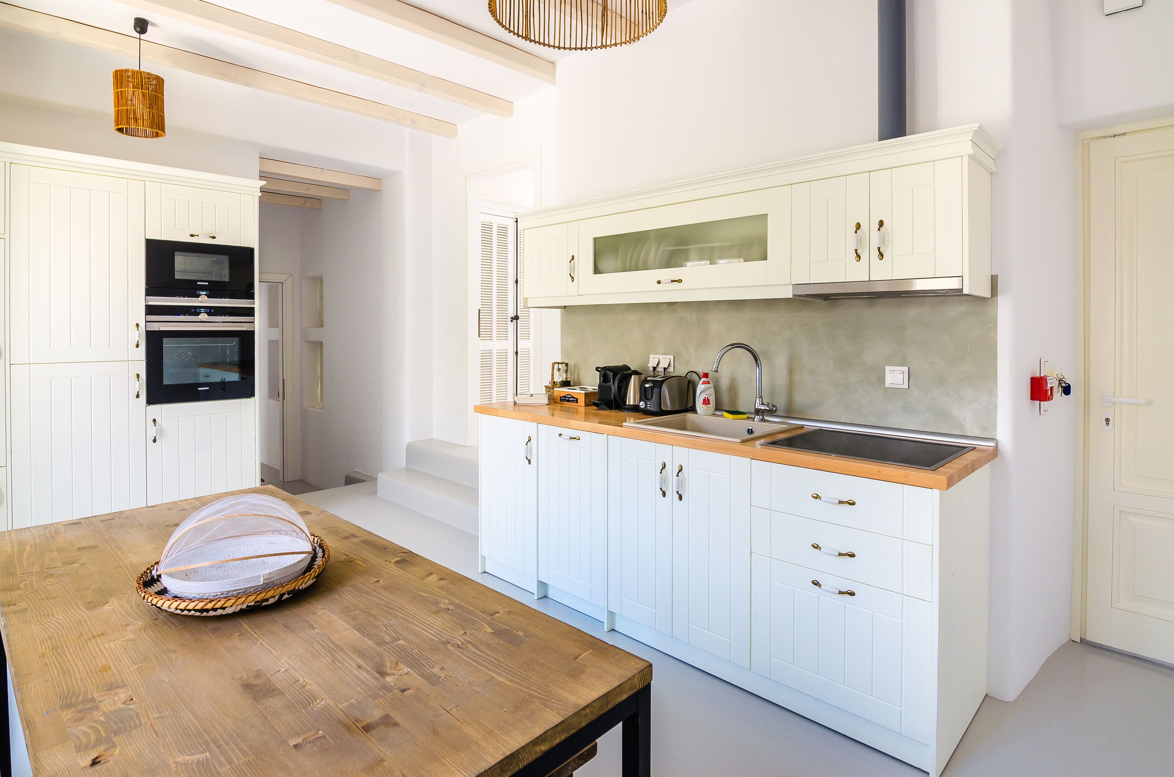 Una cocina moderna con armarios blancos, una mesa de madera y una cesta sobre la mesa.