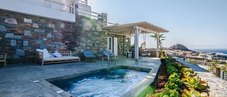 A stone-walled pool area with lounge chairs, a pergola, and a view of the sea.