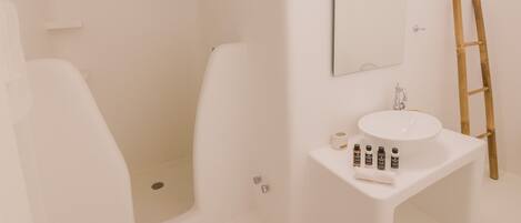 A bathroom with a white sink, mirror, and shower. There are toiletries on the sink and a ladder against the wall.