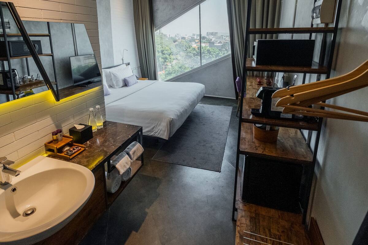 A modern hotel room with a large bed, a built-in TV, a bathroom with a sink and mirror, and a city view through the window.