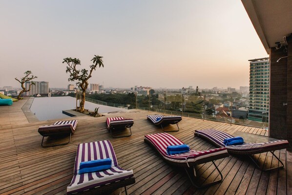 Un área de lounge en la azotea con sillones de sol y piscina, con vistas a un paisaje urbano.