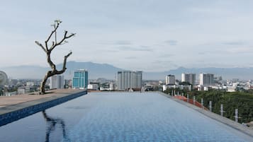 A rooftop pool with a view of a cityscape and mountains in the distance.