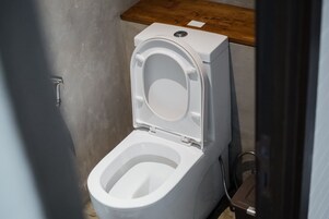 A white toilet with a closed lid, a wooden countertop above it, and a metal pipe to the right.