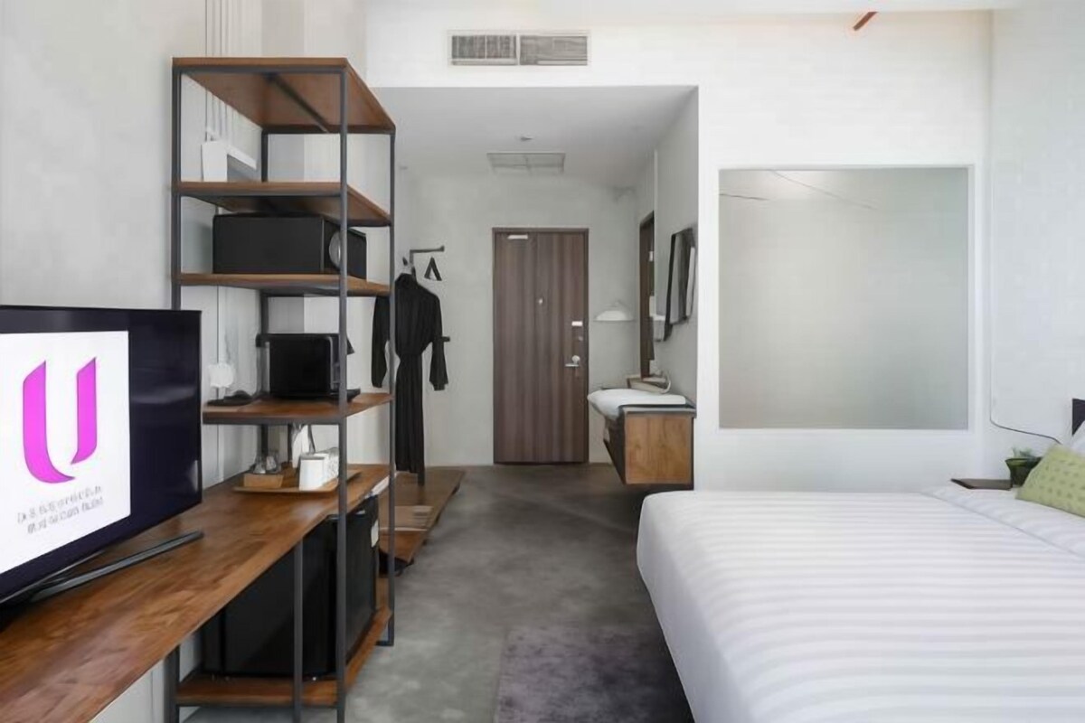 A hotel room with a bed, a desk with a computer, a wardrobe, and a television.