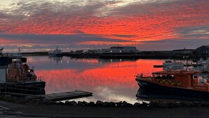 A harbor with boats docked, calm water reflecting the sky, and a clear view of the surrounding buildings. - Hvammur Apartments (Höfn)