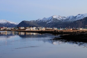 A coastal town with buildings along the shore, a calm body of water, and snow-capped mountains in the background. - Hvammur Apartments (Höfn)
