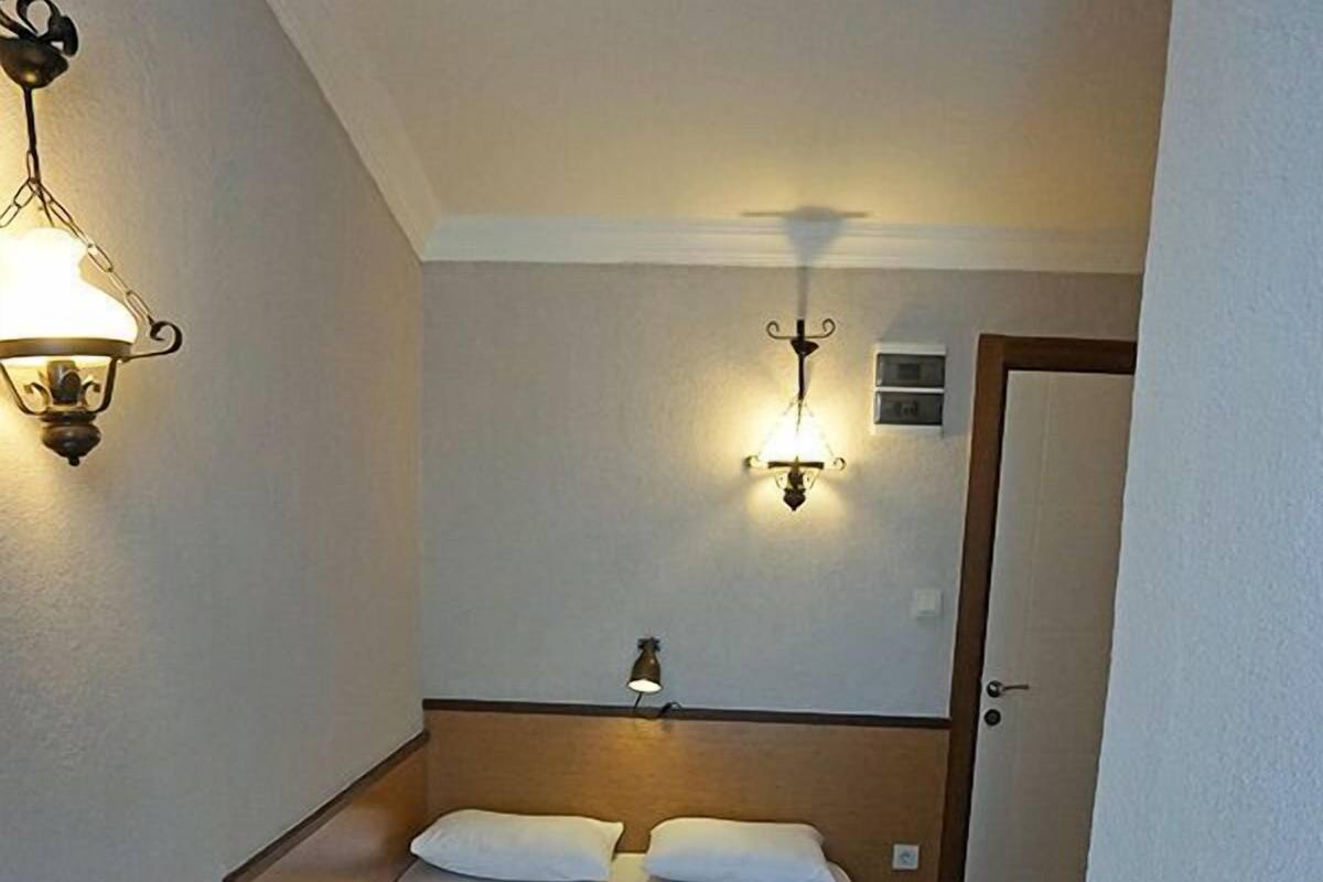A small, narrow hotel room with a single bed, two wall-mounted lights, and a radiator.