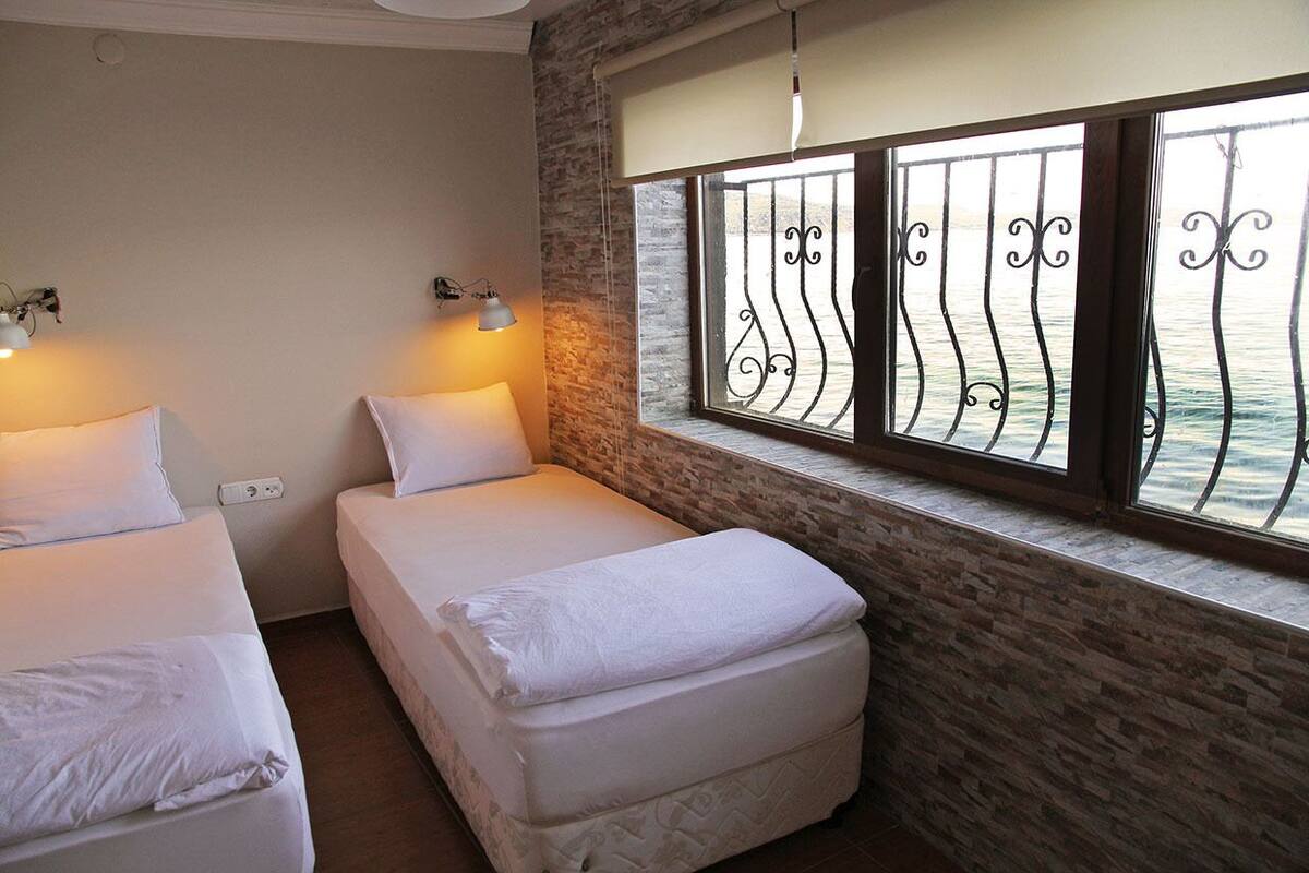 A room with two beds, a stone wall, a window with metal bars, and two wall-mounted lamps.