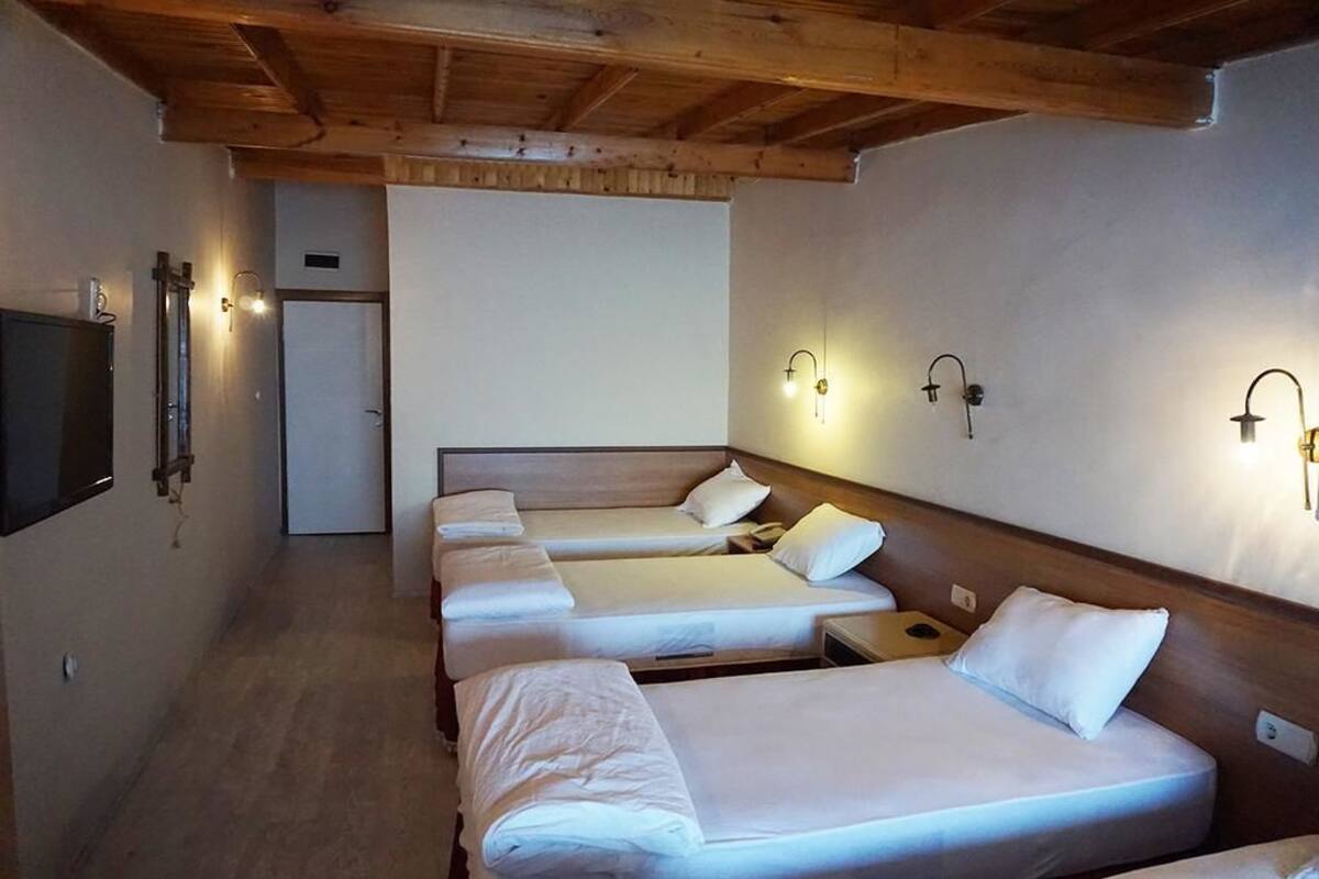 A hotel room with four single beds, wooden headboards, and wall-mounted light fixtures.