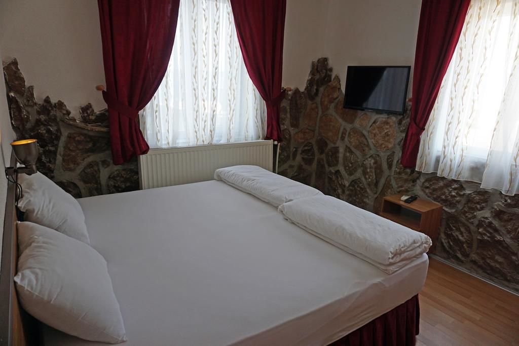 Een bed met witte lakens, rode gordijnen en een stenen muur.